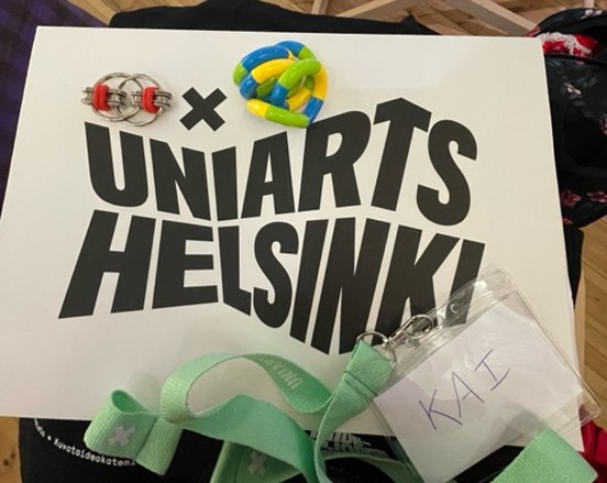 Image 3: Fidget toys placed on top of a paper file that reads ‘UNIARTS HELSINKI’, with a name tag with a lime green strap and name ‘KAI’. 