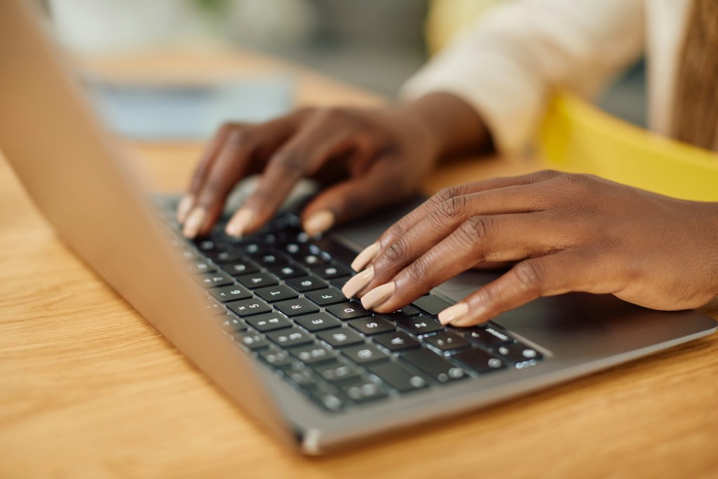 A close up of a black woman's hands typing on a laptop