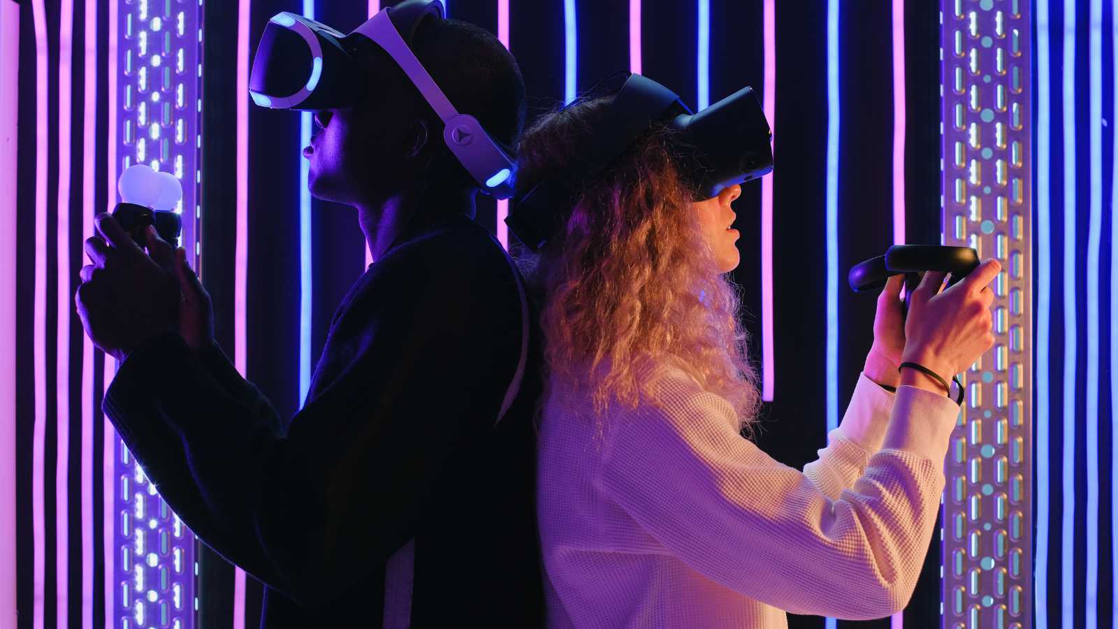 Virtual reality. A young black man and a young white woman stand back to back holding virtual reality controllers in their hands and wearing virtual reality goggles on their heads.