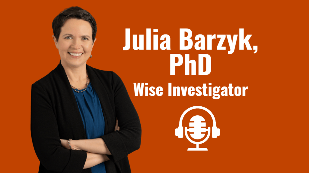 Dr. Julia Barzyk of Wise Investigator featured interview guest on The Social Academic. Julia is standing with her arms lightly crossed. She is smiling widely wearing a black suit and French blue top.