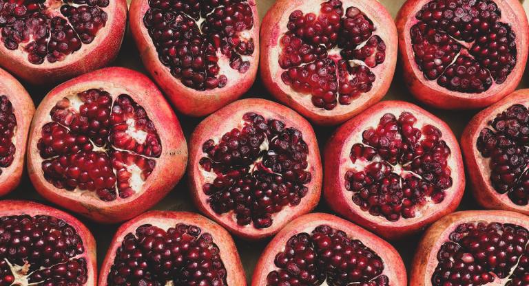 12 pomegranates side by side with the top sliced open to reveal many bright juicy seeds inside.