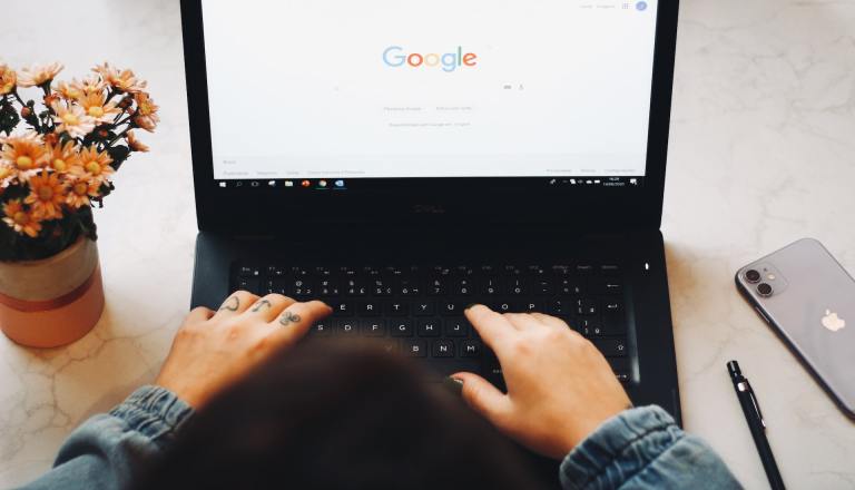 An overhead view of a person working on a laptop. They have the Google Search page pulled up and are starting to type in their search query.