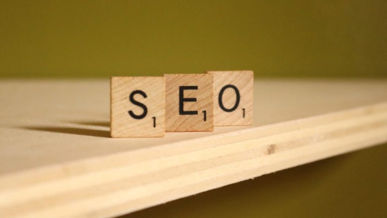 Scrabble letters that spell out 'S' 'E' and 'O' stand facing the camera on a shelf. SEO is an acronym for search engine optimization.