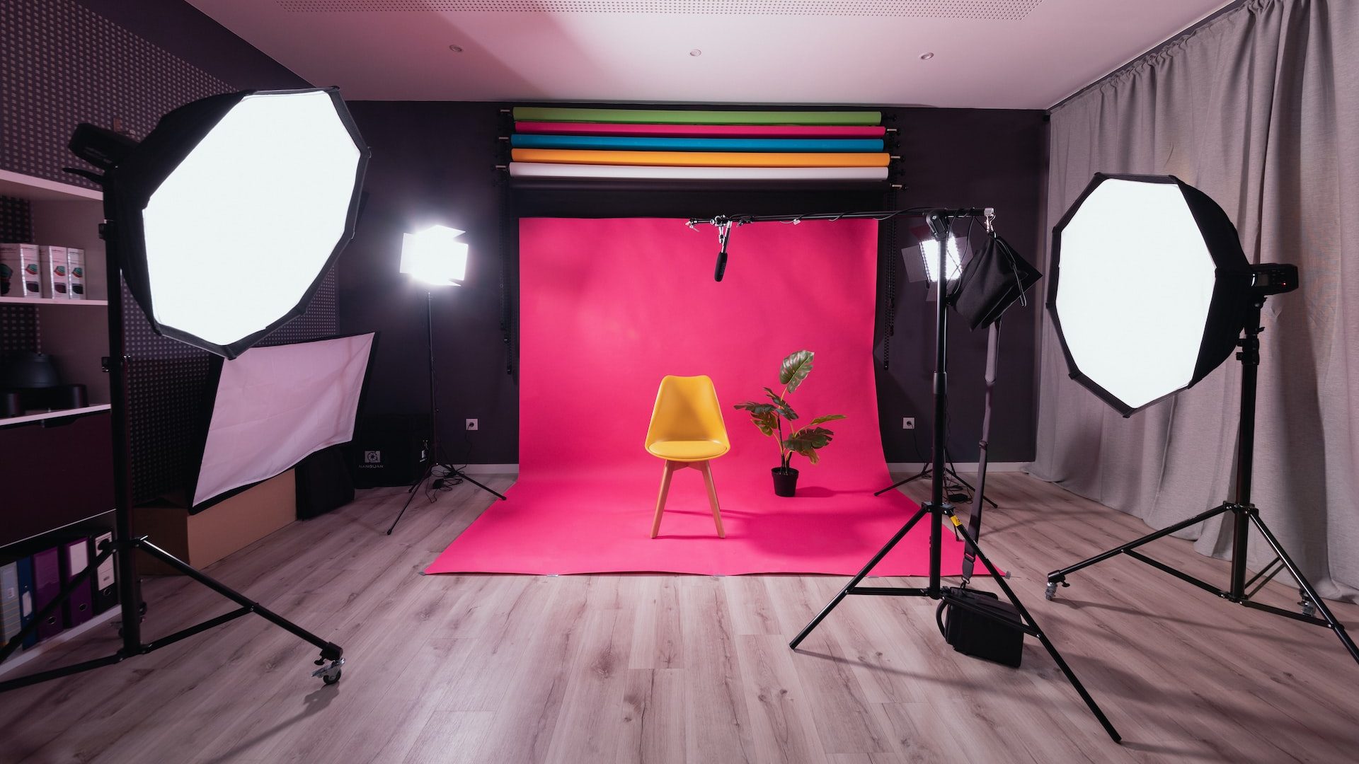 Photography and video production studio with a yellow chair, plant, and pink backdrop. There are large lights on tripods.