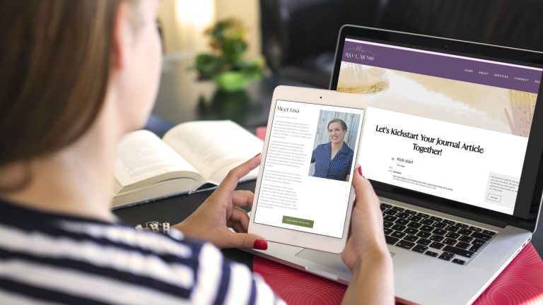 Over-shoulder view of woman in striped shirt holding a tablet. On the tablet is a bio and photo of Dr. Lisa Munro. Behind the tablet on a table is an open book and an open laptop. On the laptop is Lisa's website with a page open that reads 'Let's Kickstart Your Journal Article Together!' for her upcoming academic article writing workshop.