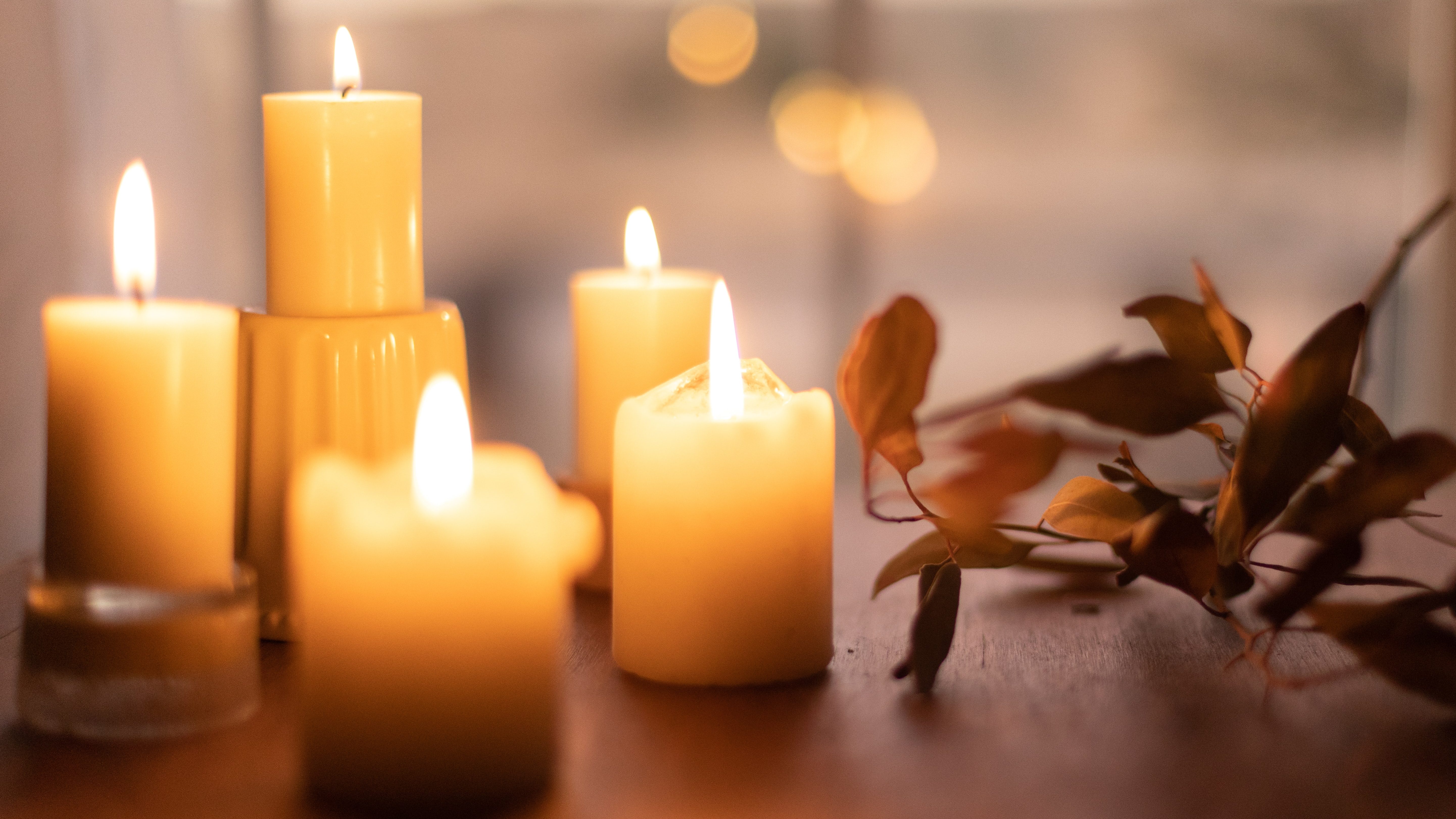 Five white candles on a table next to a dead branch