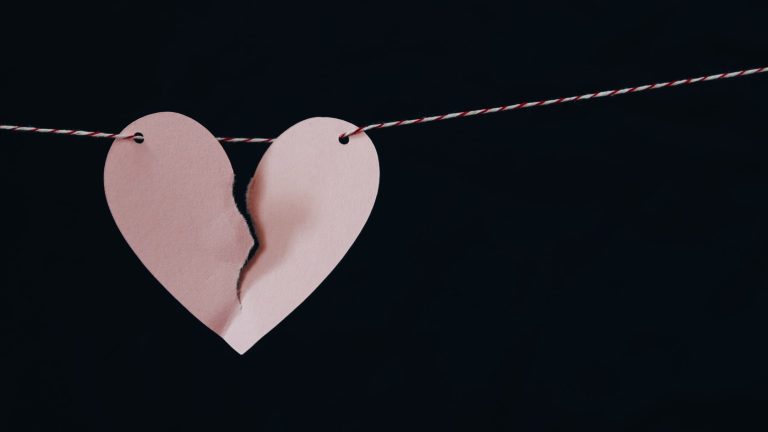 A paper cut out heart is broken down the center. The rip goes through about 2/3 of the heart. A red and white thread is strung through two holes on either side of the heart to hold it up.