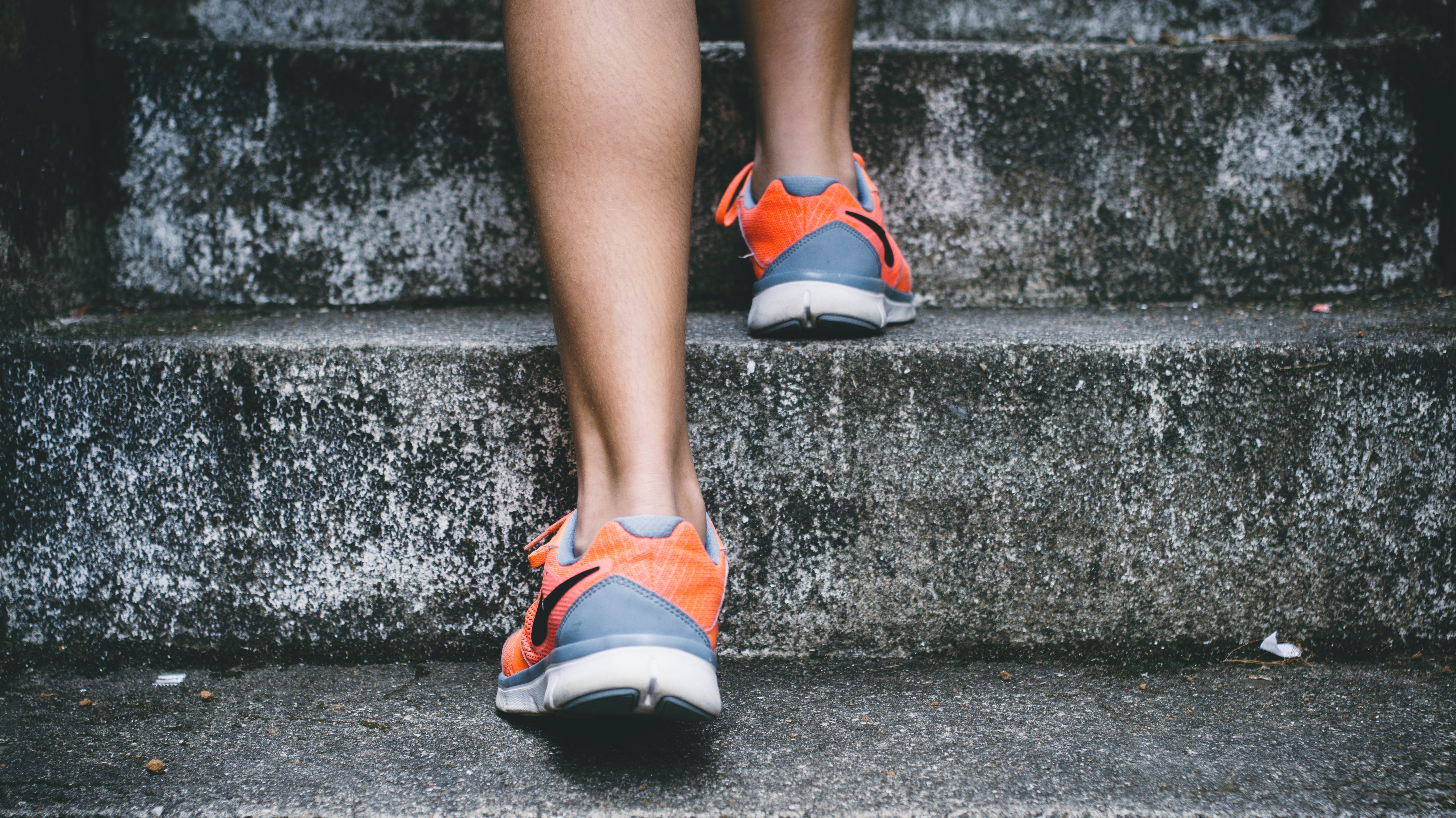 A woman wearing running sneakers walks up concrete stairs