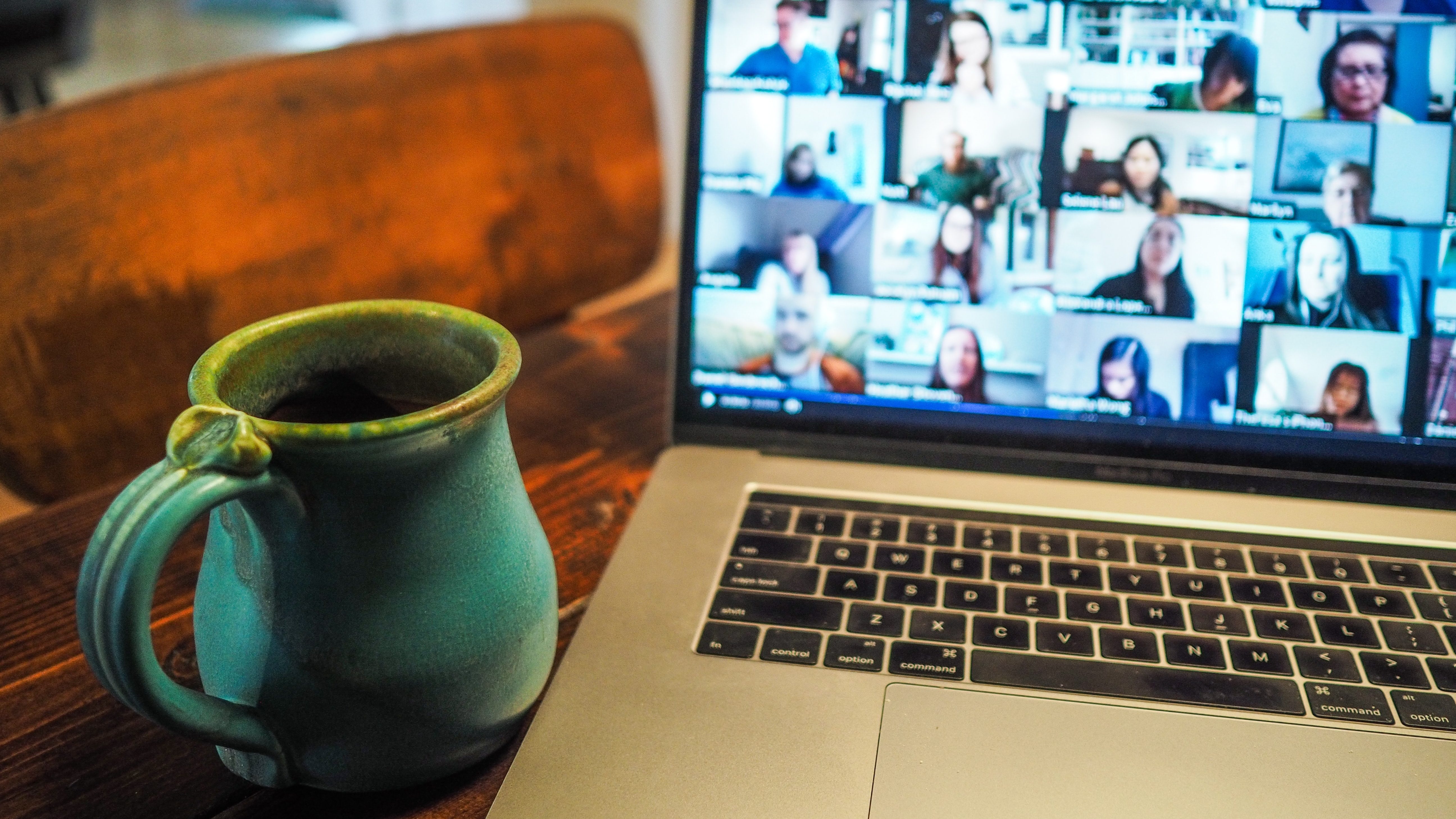 A green mug next to an open laptop with a large group Zoom meeting on the screen.