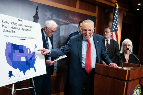 Senator Chuck Schumer points to a poster board showing a map of the United States with the title "Trump-voting states have more to lose if Education Department dismantled."