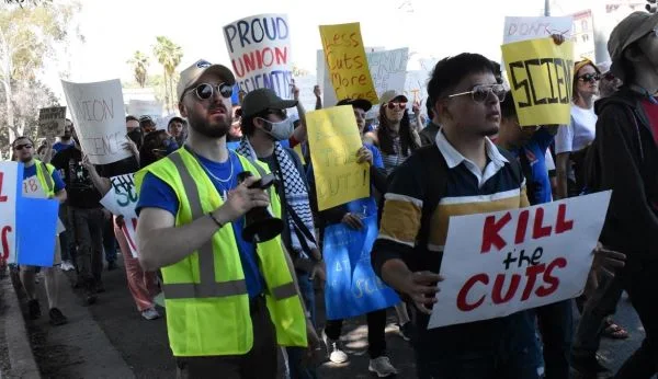 Large group of marching protesters with signs that say "Kill the Cuts"