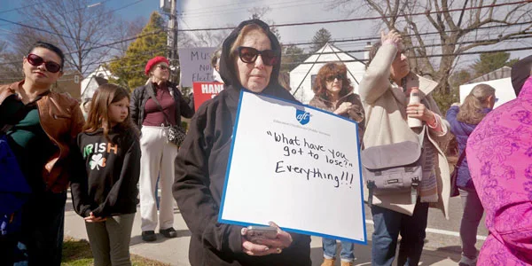 Woman standing in a crowd with a sign that reads "What have you got to lose? Everything"
