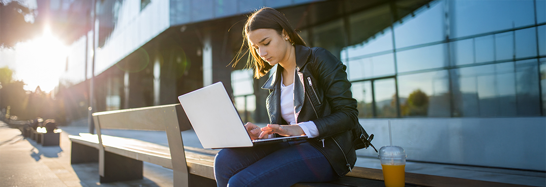 A woman sitting on a bench uses her laptop.