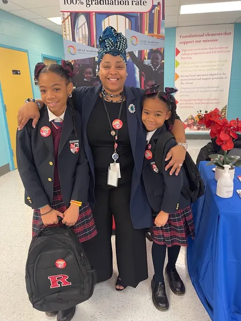 An adult stands with two students in a school hallway. Everyone is looking at the camera