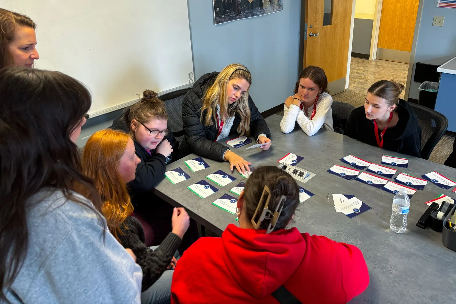 High school students sit around a table while reading documents and collaborating together.
