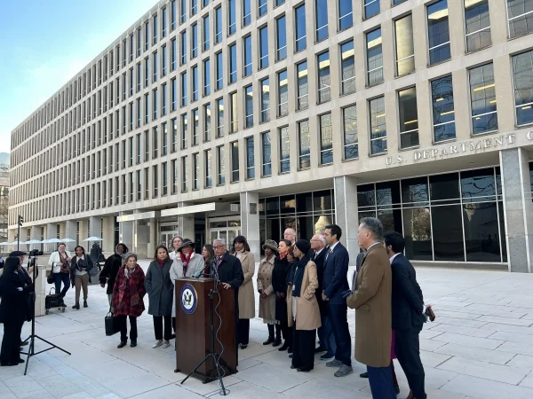 Lawmakers stand at a podium outside the Education Department building, dressed for winter.