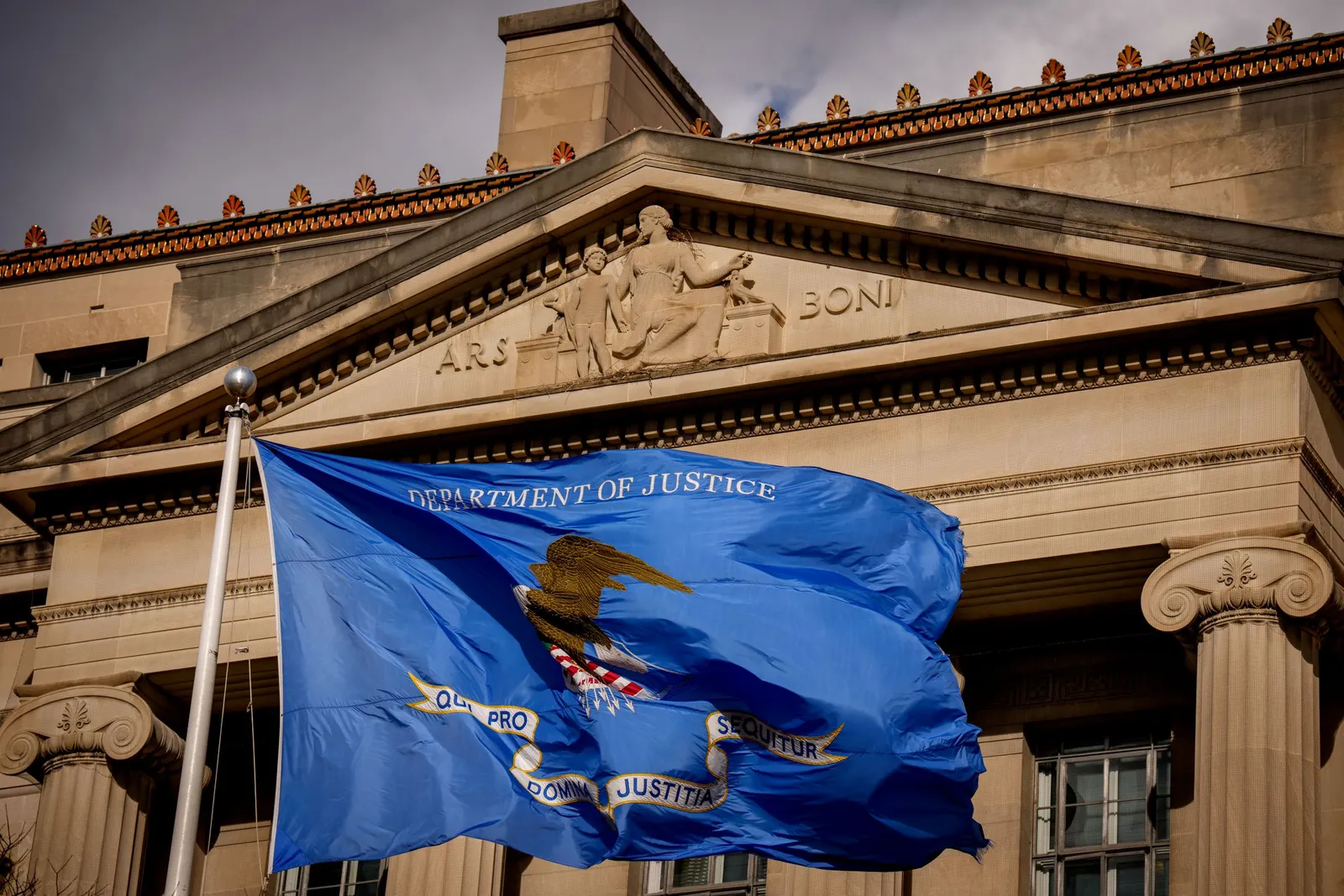 A blue flag that says "Department of Justice" waves in front of the agency's building.