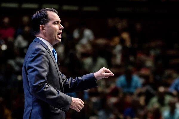 Wisconsin governor and republican presidential candidate Scott Walker speaks to voters at the Heritage Action Presidential Candidate Forum September 18, 2015 in Greenville, South Carolina. He is a white man with dark hair shaped into a severe widow's peak, wearing a suit and photographed in profile.
